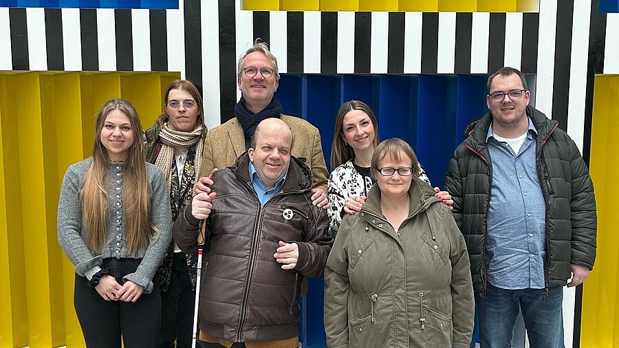 Einige KIB Mitglieder posieren vor einer gelb blauen gekachelter Wand