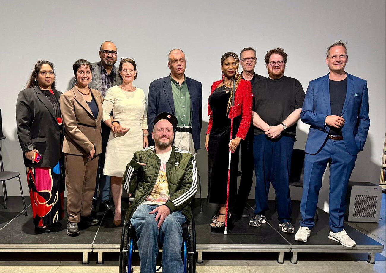 Die Teilnehmenden der Podiumsdiskussion stehen auf einer Bühne